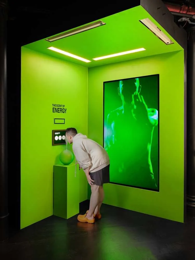 A visitor leans in to smell a green sphere in a lime-green booth labelled The Scent of Energy.