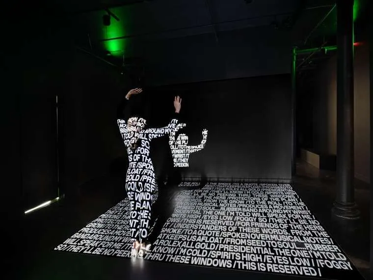 Poem text projected over a dancer and across the floor in a dark room.