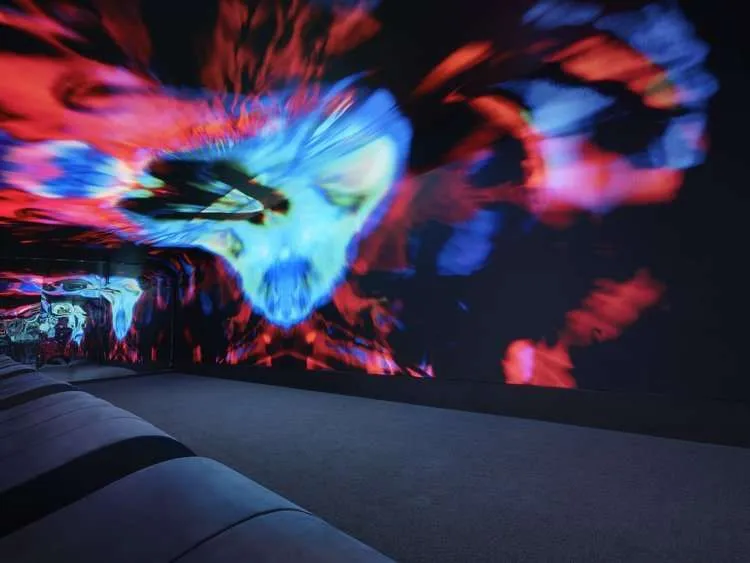 An empty lounge with low seating beneath a wall-to-ceiling psychedelic projection.