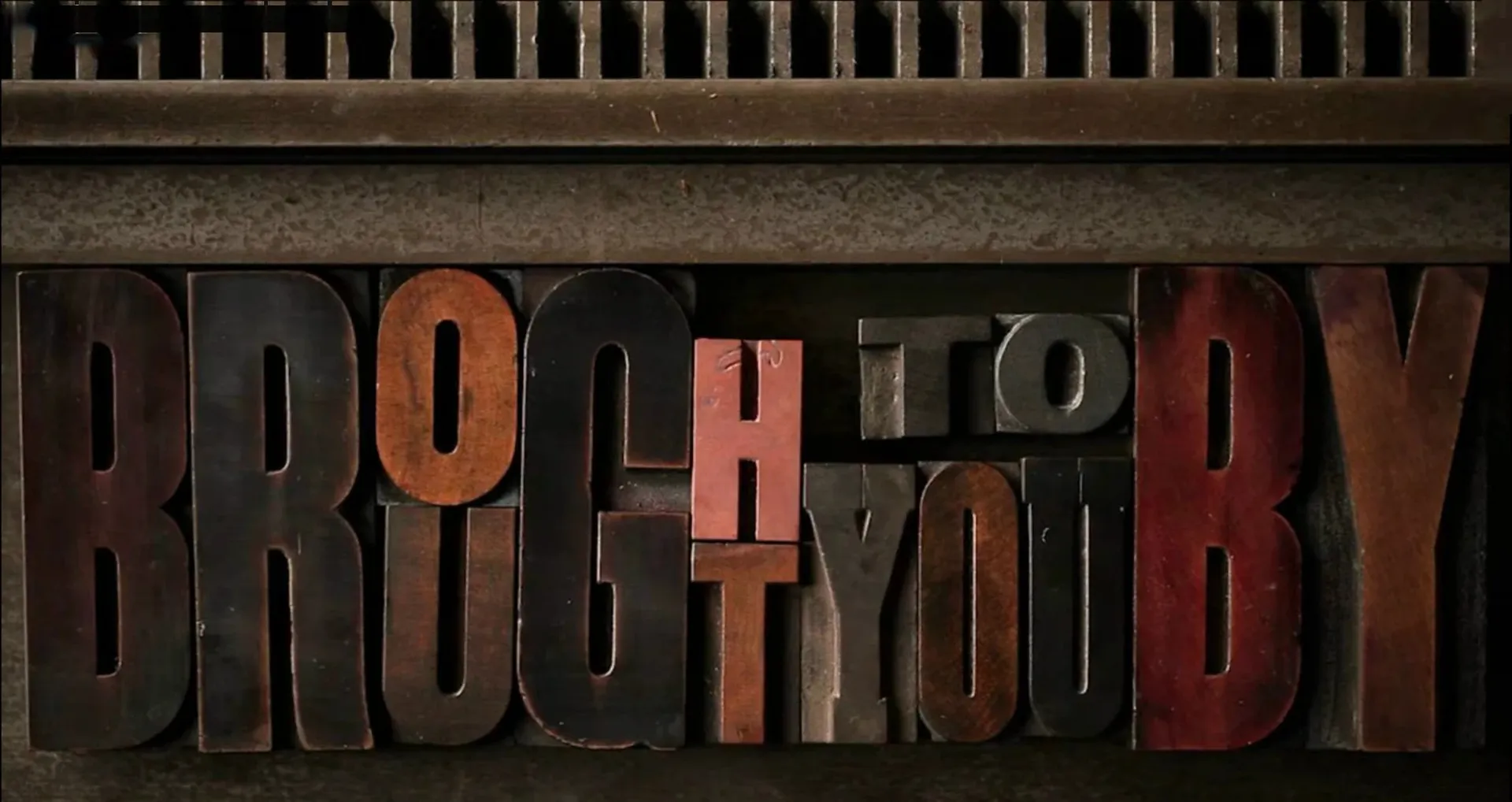 Worn wooden letterpress type spelling Brought To You By, set in a type tray.