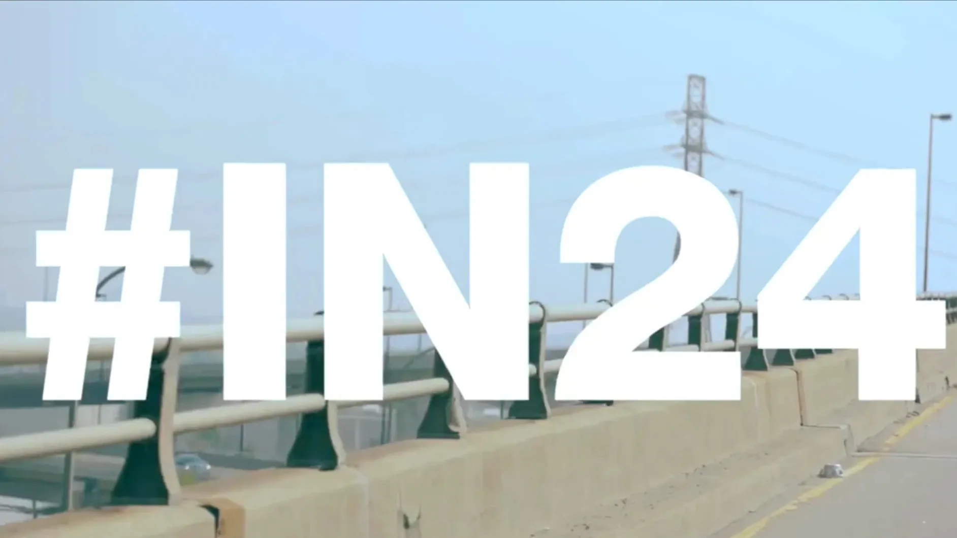 The hashtag #IN24 in giant white letters over a highway overpass, a hydro tower against a hazy sky.