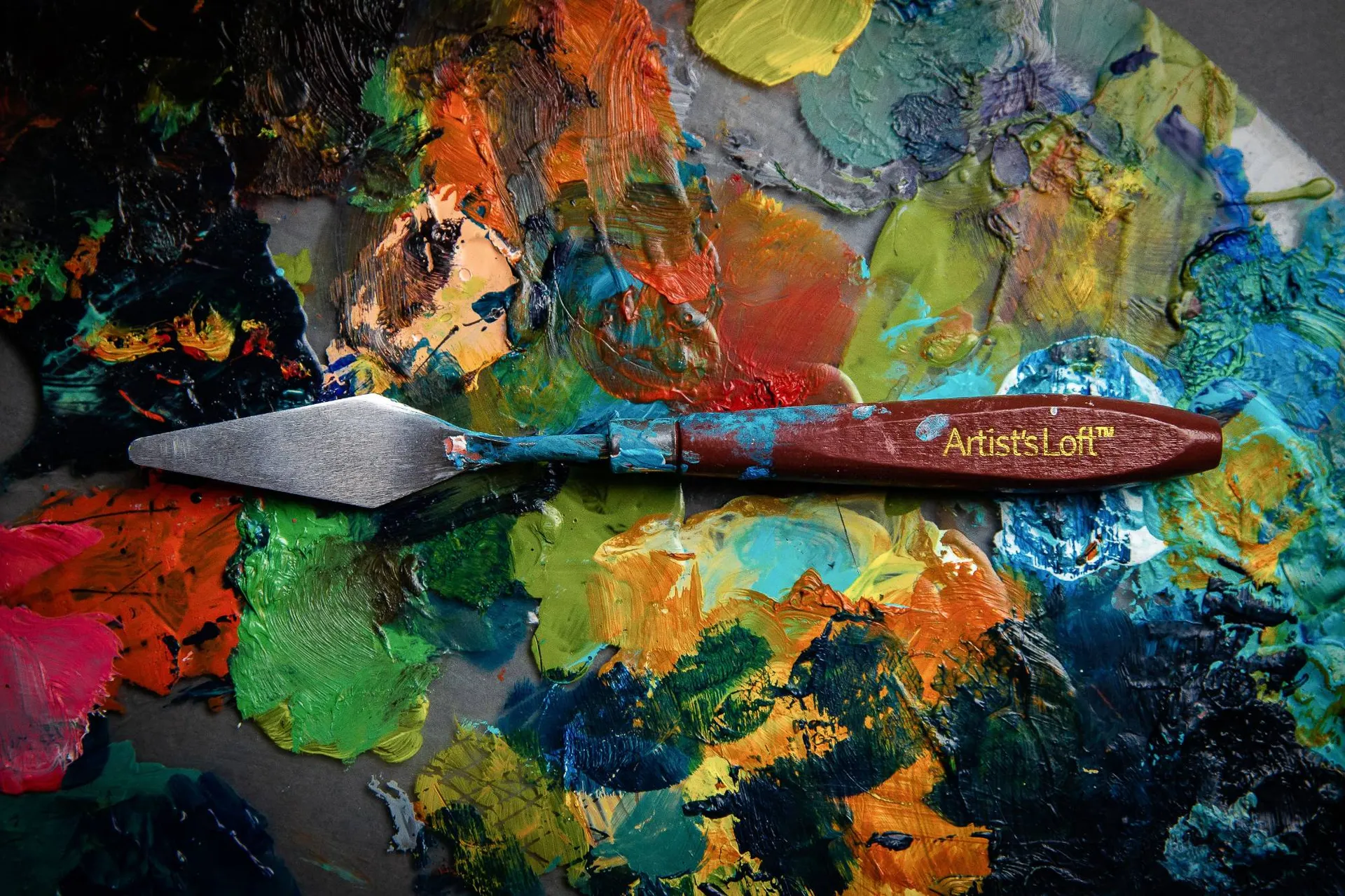 An Artist's Loft palette knife resting on a thickly painted palette.