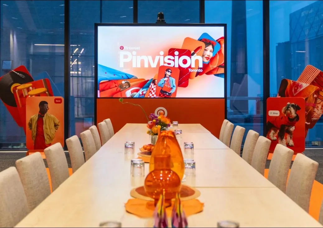 A long boardroom table set with orange glassware and florals, the Pinvision Toronto screen at the end flanked by oversized Pin cut-outs.