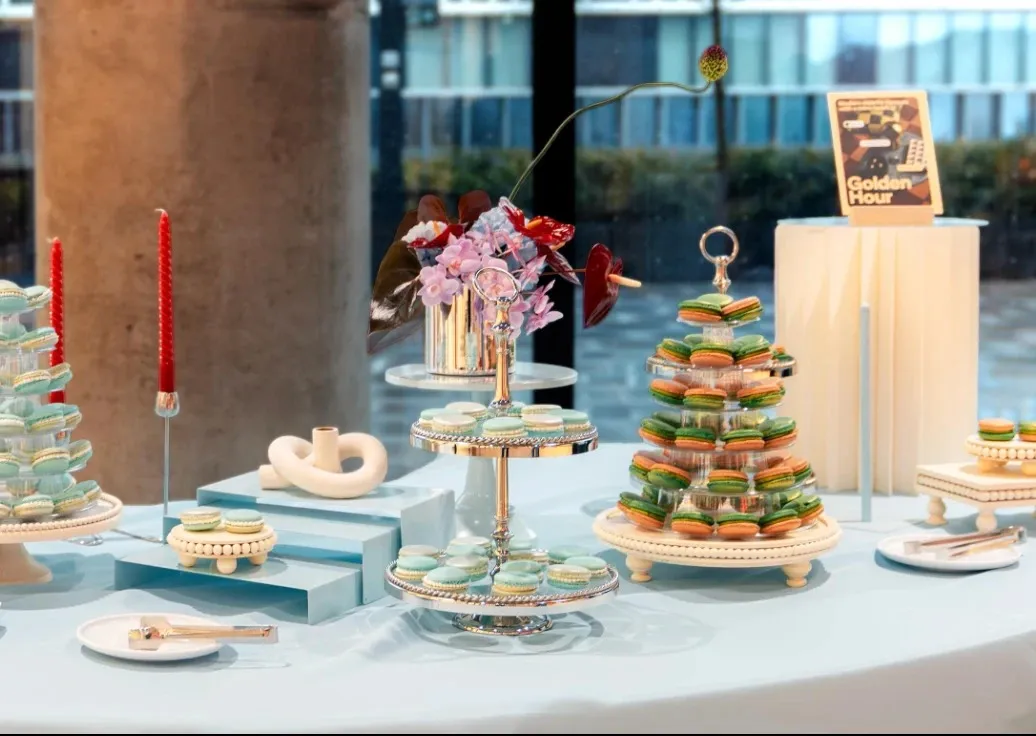A dessert table of mint and orange macarons on tiered stands, red candles and orchids, with a Golden Hour sign.