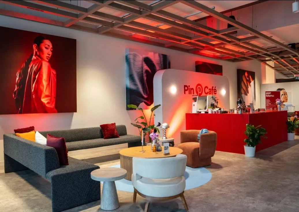The Pin Café lounge: a red coffee bar, a grey sofa and armchairs, and large red-lit portraits on the walls.