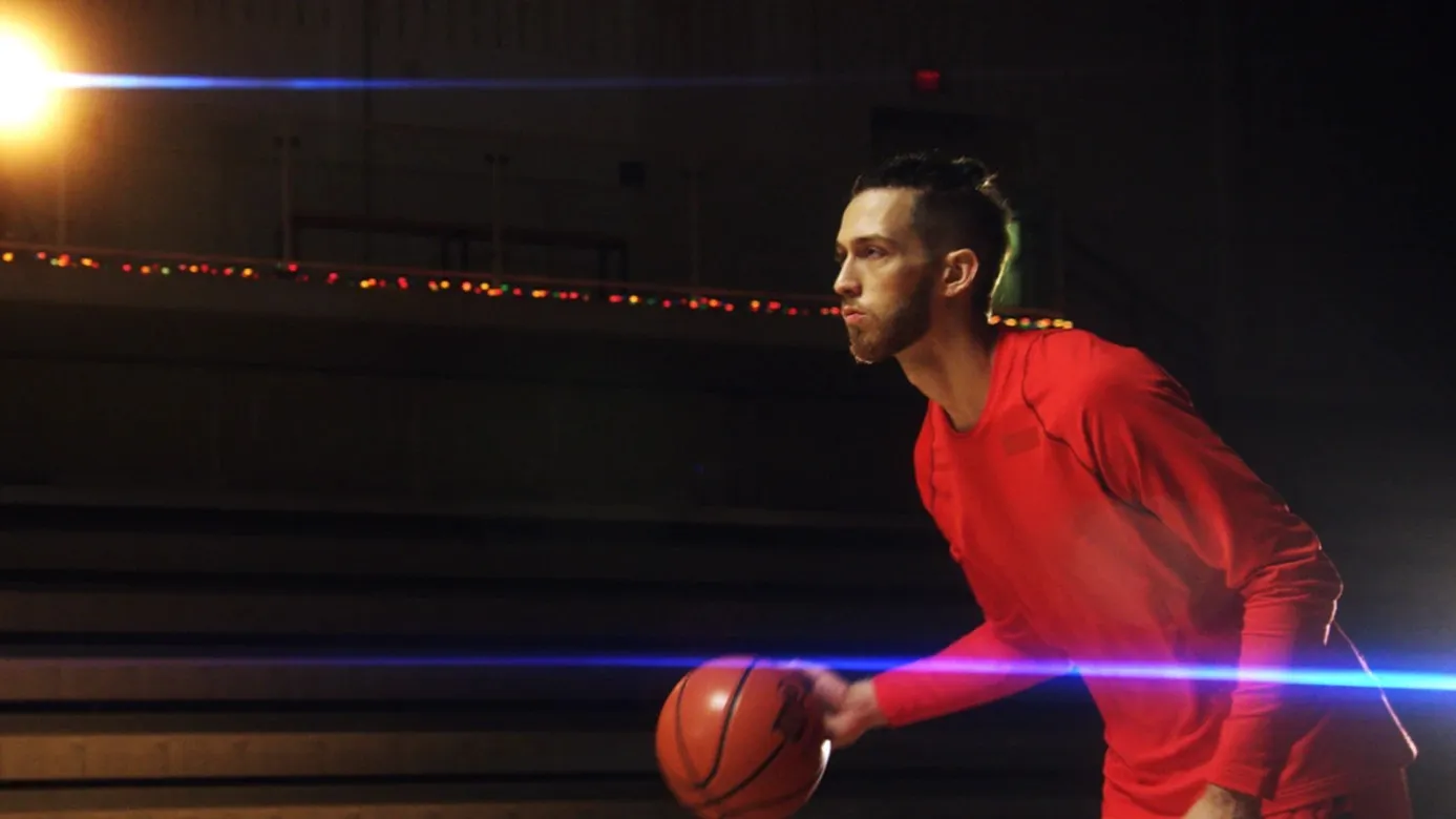 A basketball player in red dribbles in a dark gym, blue light streaks crossing the frame.