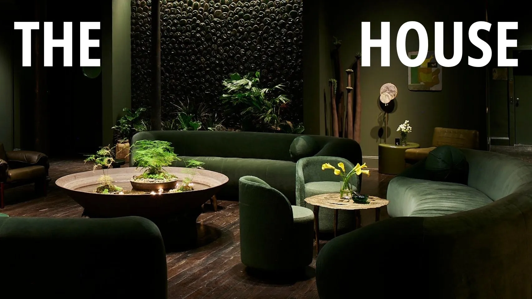 The House: a dark lounge with curved green velvet sofas around a candlelit planted fountain.